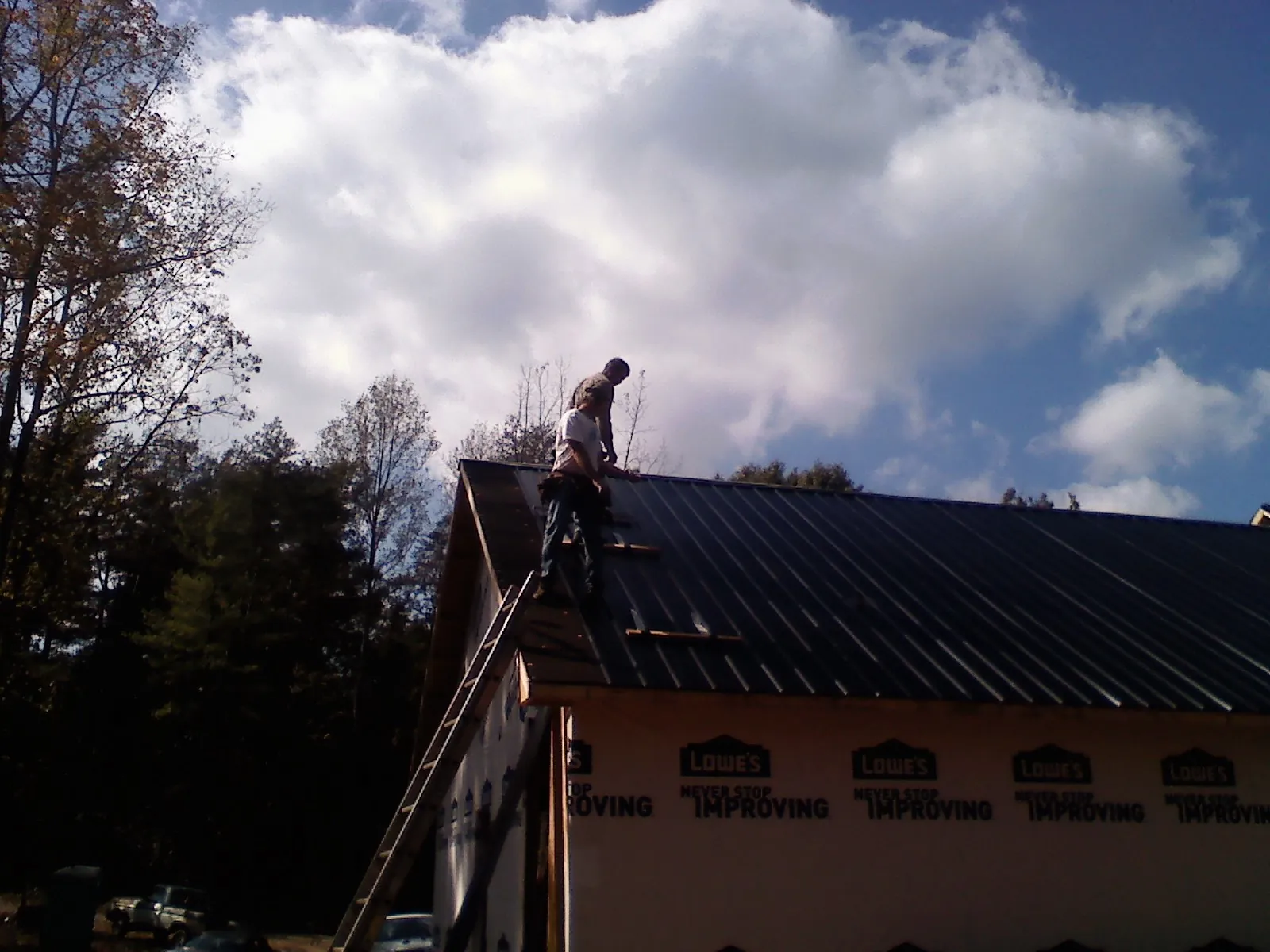Roofer fastening dark metal panels high against a cloudy sky, from a Roof Inspection job in Fairfield